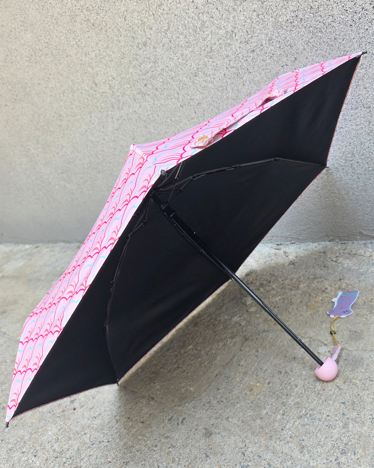 Black lining umbrella with pink patterned canopy on a concrete surface