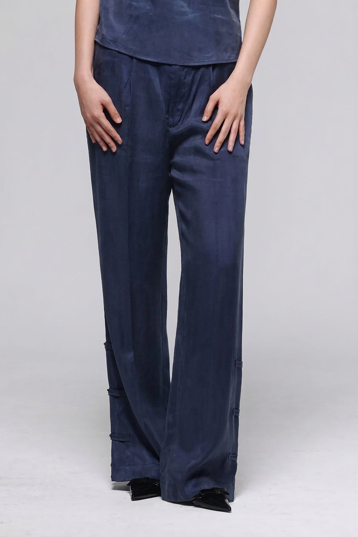 A person wearing dark navy wide-leg pants with a matching top, standing against a light gray studio background.