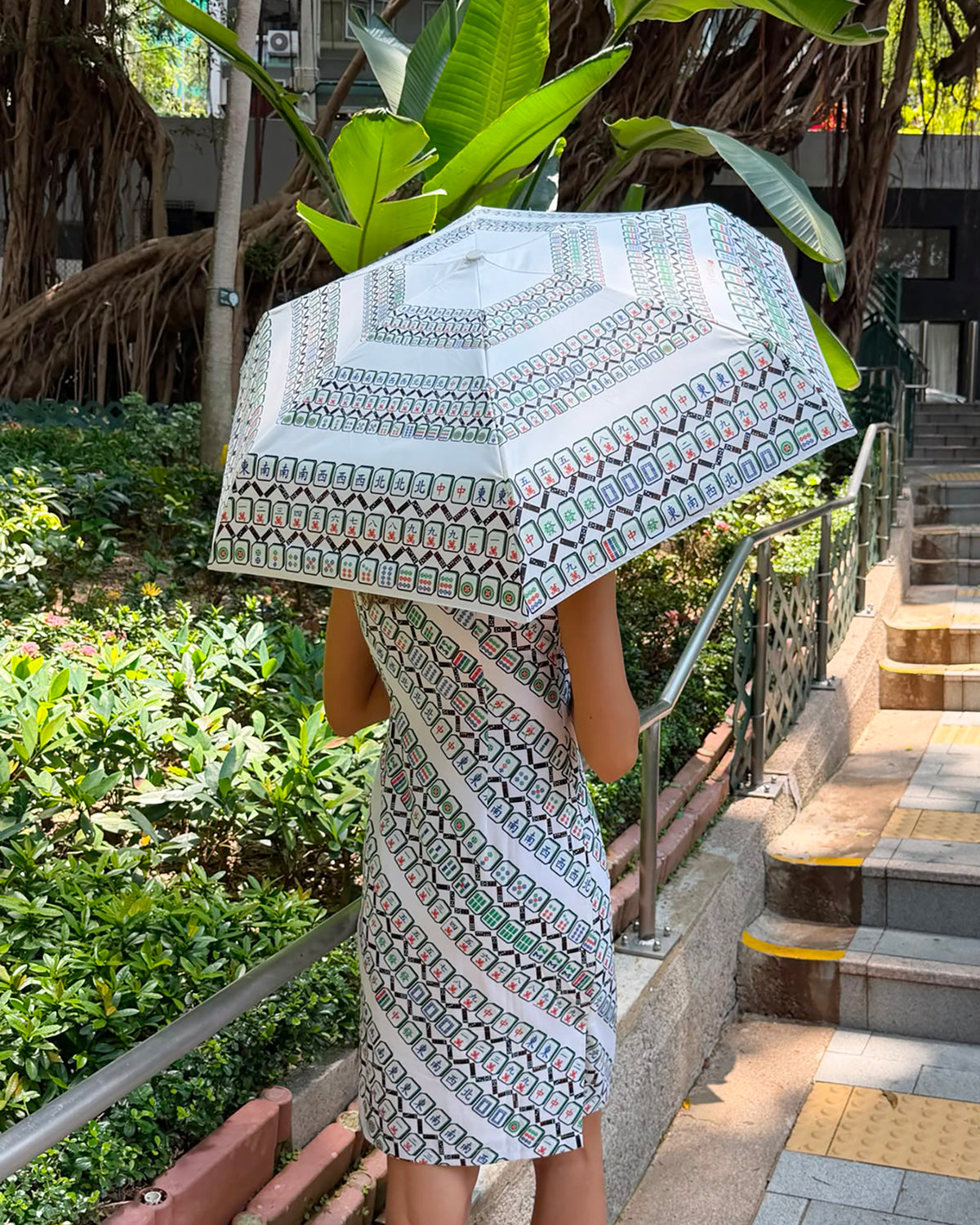 Person holding a patterned umbrella in an outdoor setting with greenery and steps.