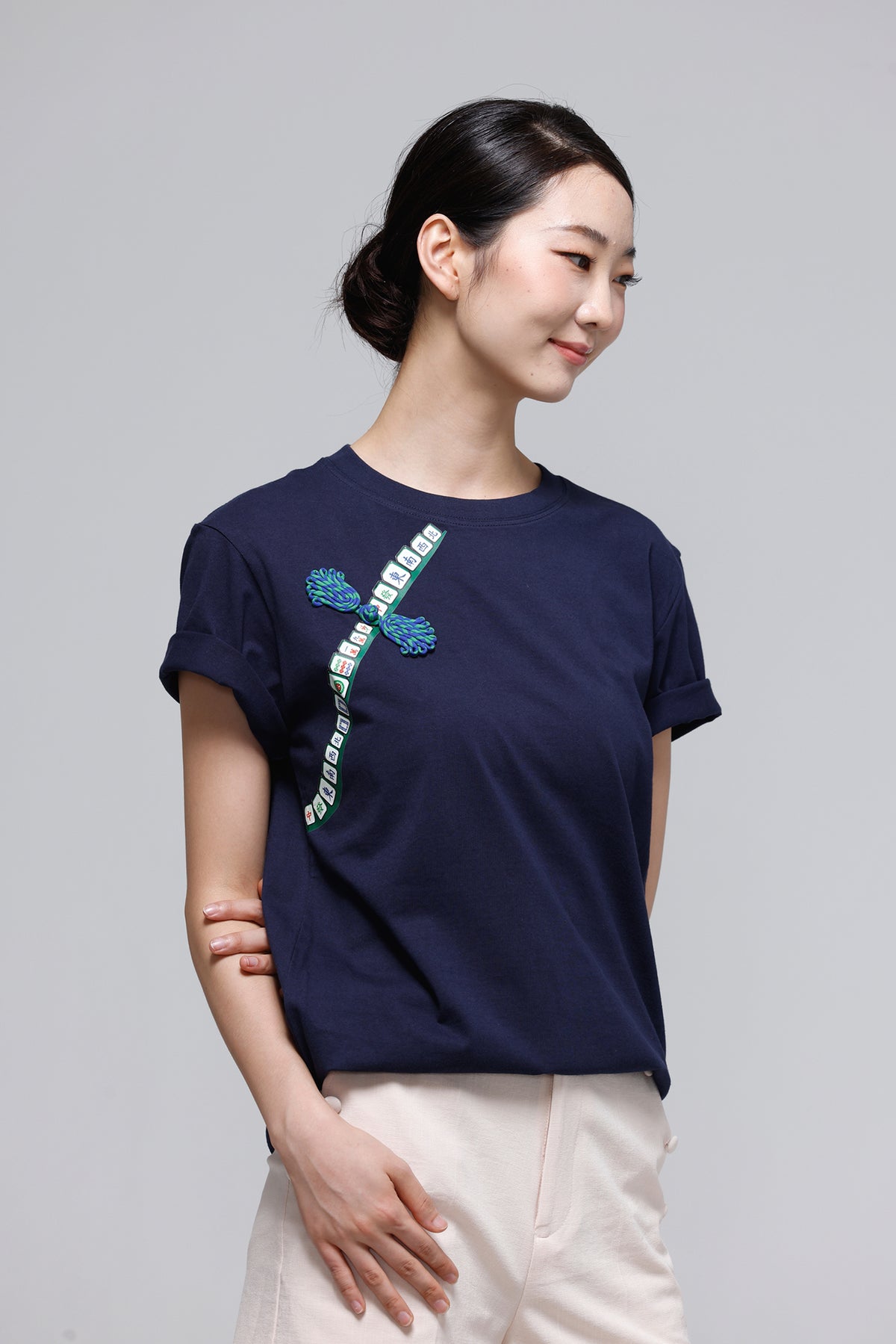 A woman wearing a navy blue short-sleeve t-shirt with a green and white graphic print on the front, paired with light beige pants, set against a plain light gray background.