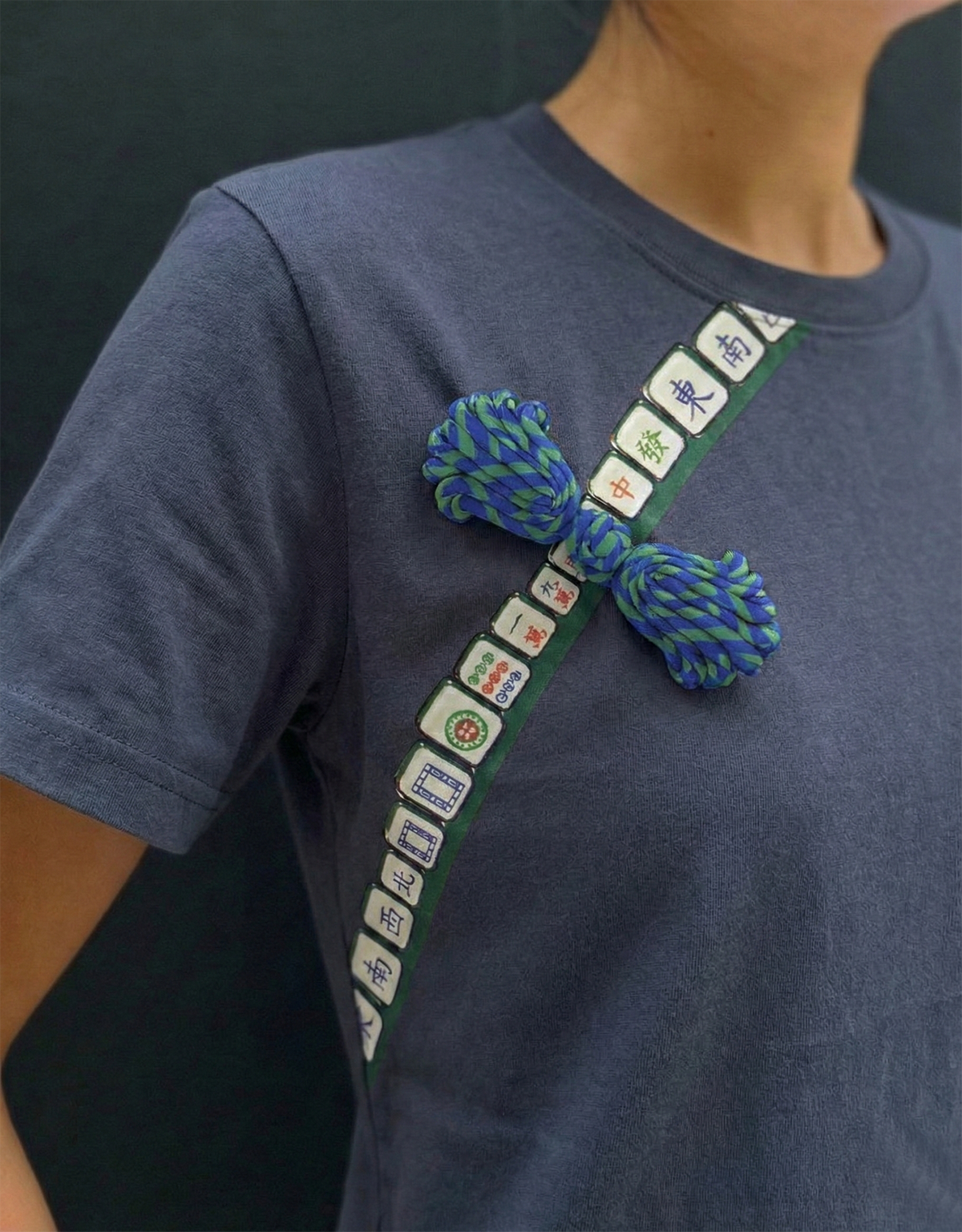 Person wearing a gray t-shirt with a decorative strap featuring Chinese characters and colorful pom-poms.