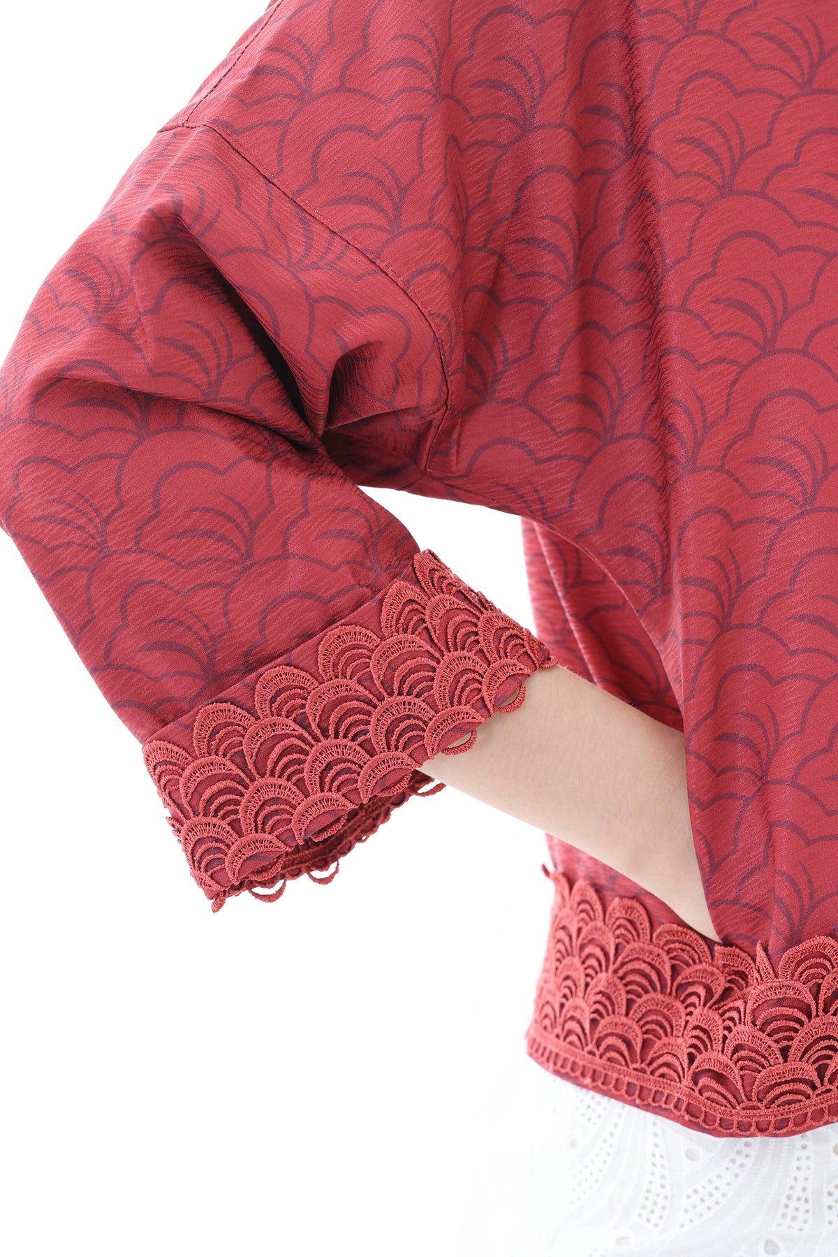 A close-up of a red patterned blouse with a scalloped lace cuff, worn by a model against a white background.