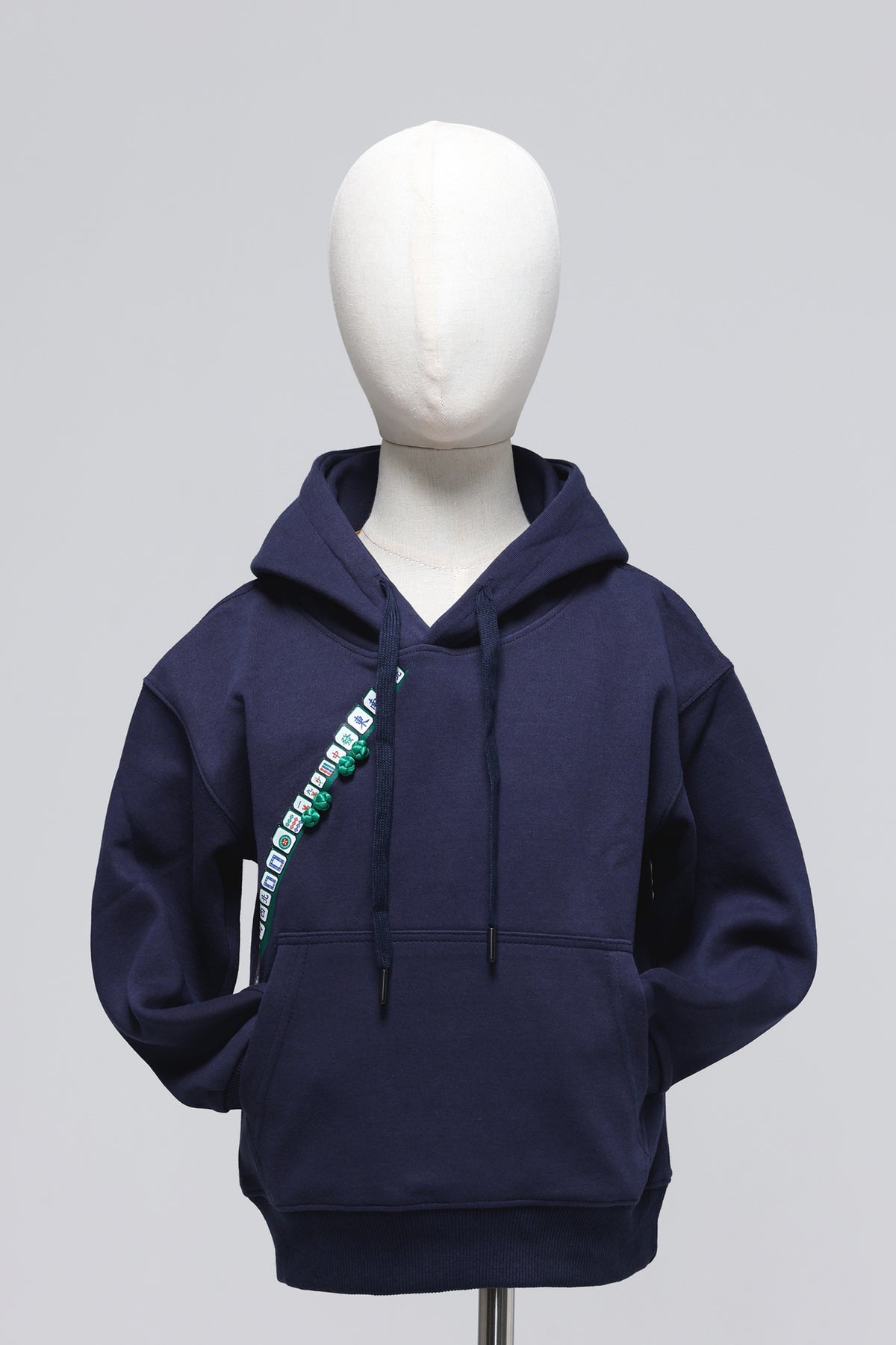 A navy blue pullover hoodie displayed on a white mannequin torso against a light gray studio background. The hoodie features a diagonal graphic print on the left chest with green and white text and a small circular logo.