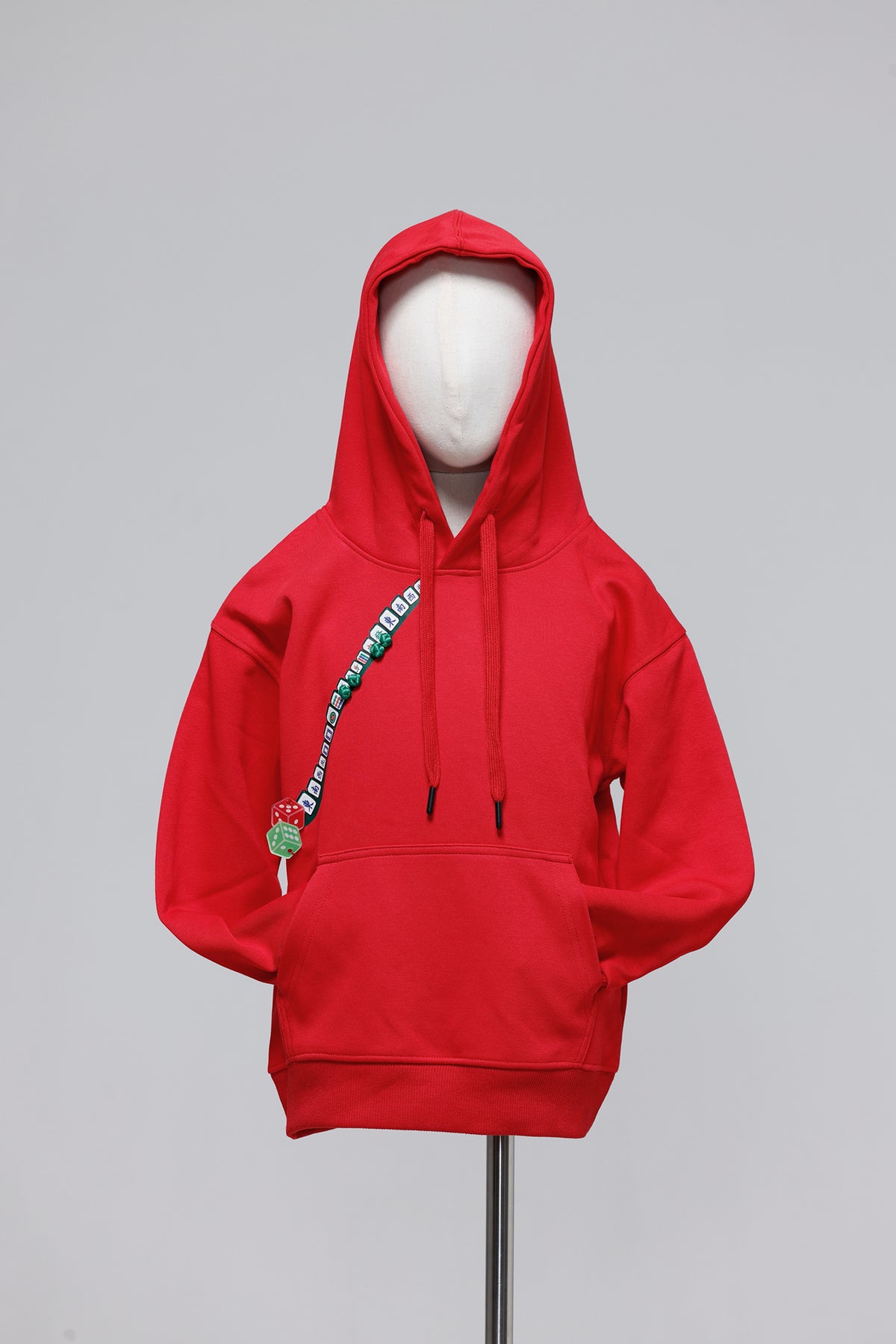 A bright red pullover hoodie displayed on a white mannequin torso against a light gray studio background. The hoodie has black drawstrings, a front kangaroo pocket, and a diagonal green graphic print with white text across the chest.