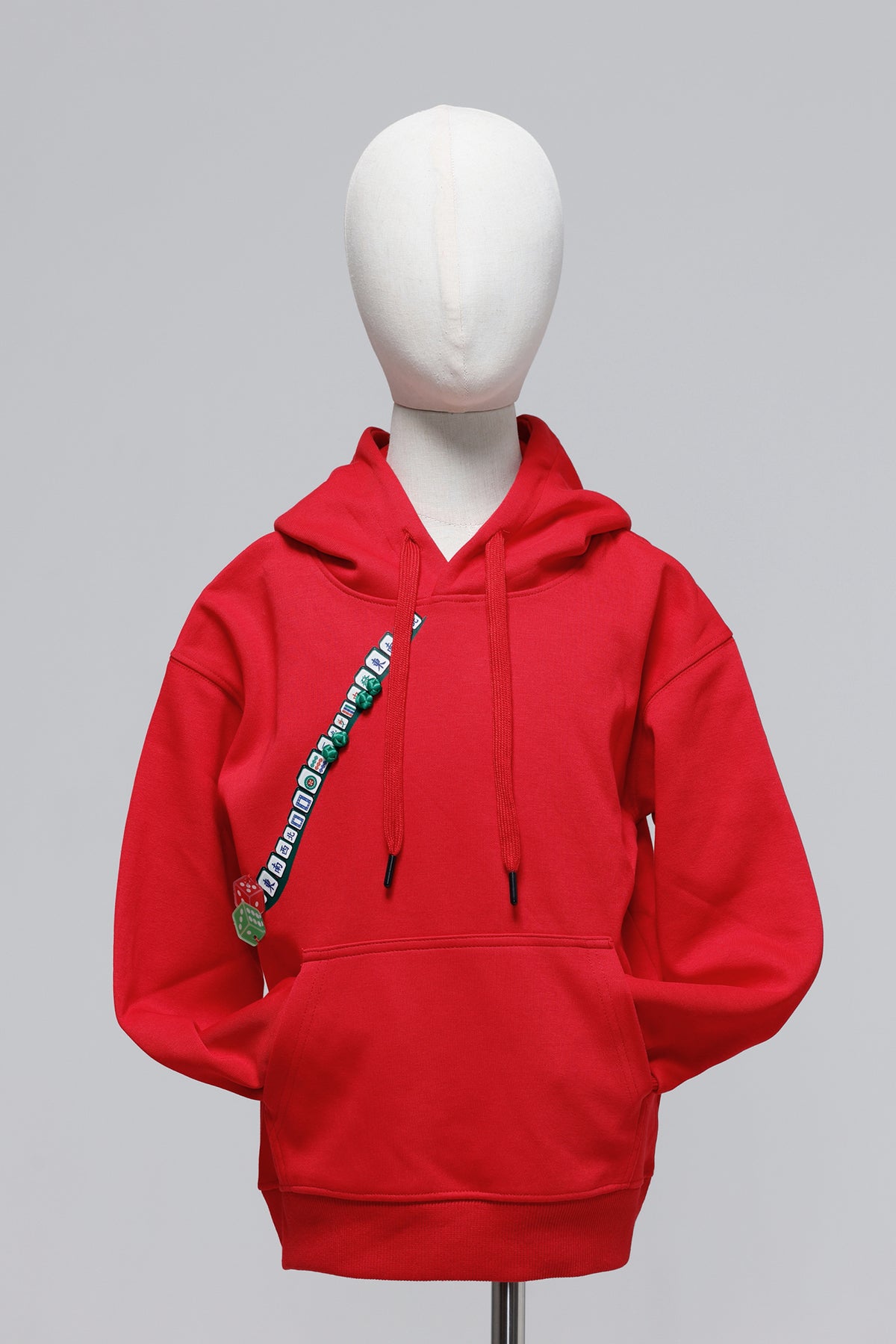 A bright red pullover hoodie displayed on a white mannequin torso against a light gray studio background. The hoodie has black drawstrings, a front kangaroo pocket, and a diagonal graphic print running from the chest toward the lower torso with green, white, and black lettering.
