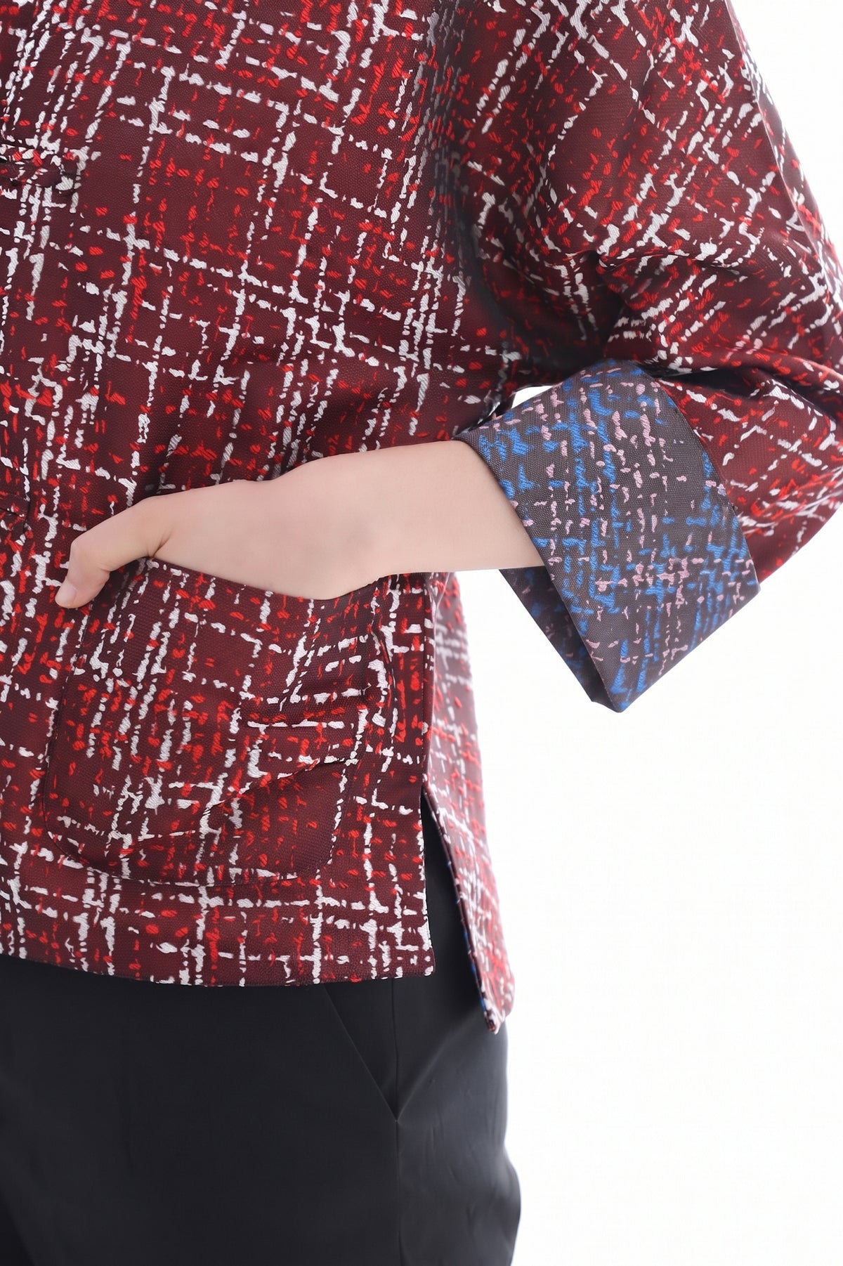 A close-up of a person wearing a patterned red and black jacket with white and blue accents, paired with black pants, against a white background.