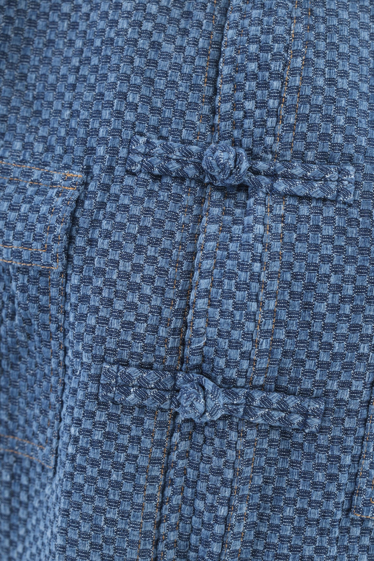 Close-up of a textured blue woven fabric garment with traditional Chinese-style tie closures and contrast stitching.