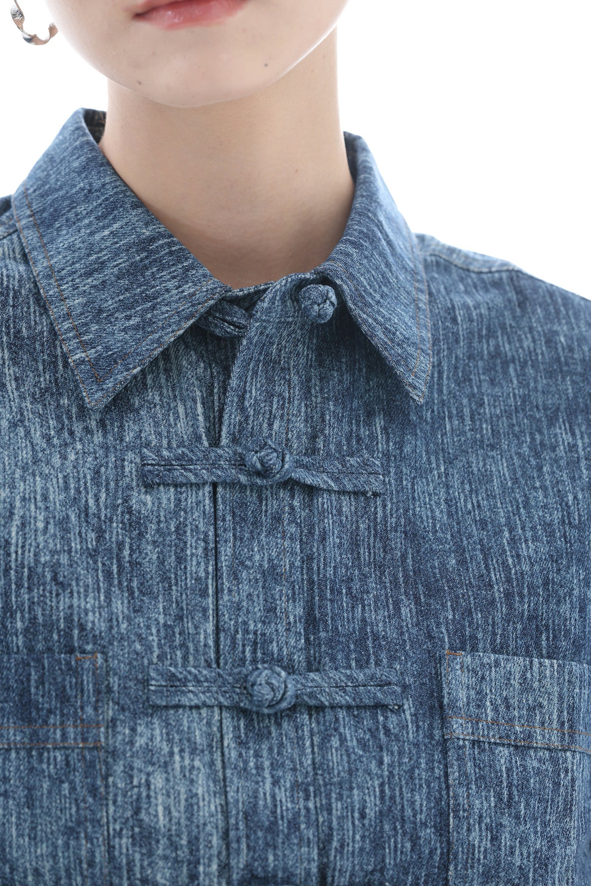 Close-up of a person wearing a textured blue collared shirt with traditional Chinese frog closures and contrast stitching.