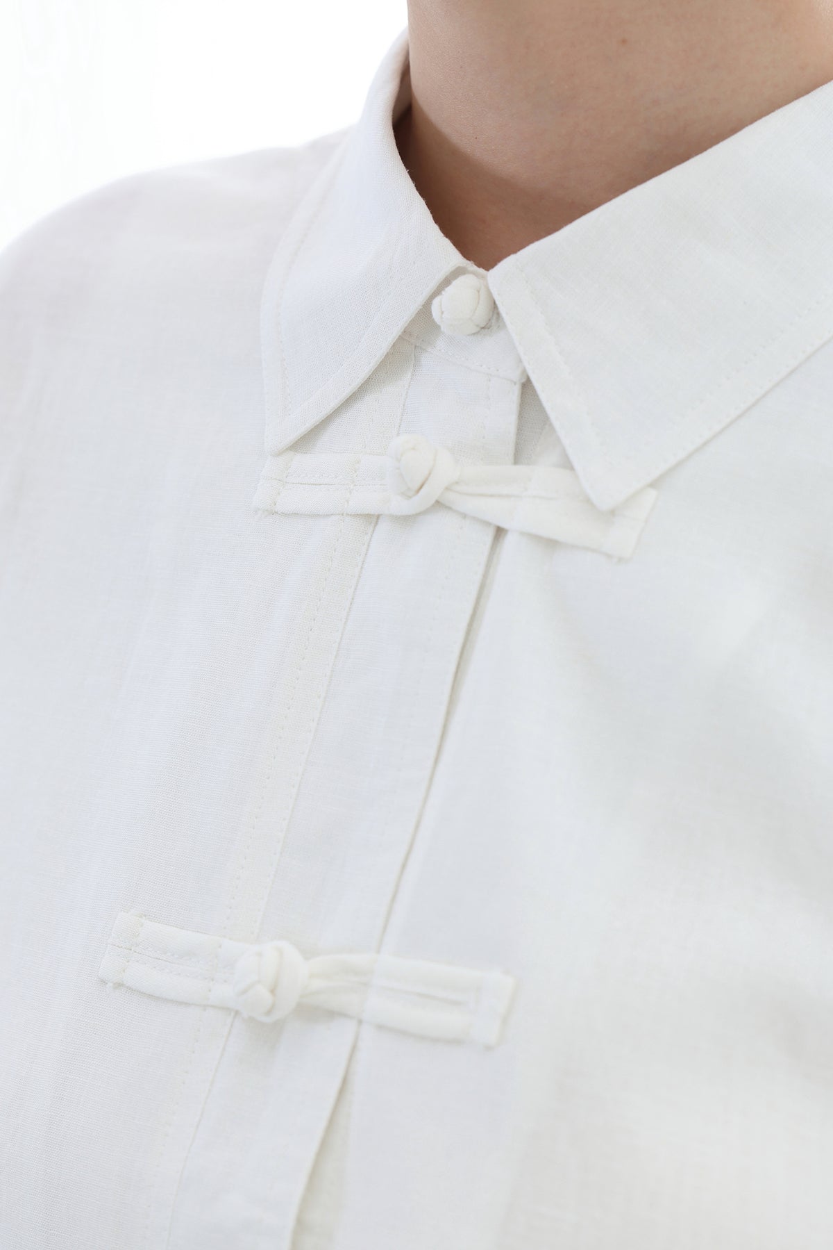 Close-up of a white collared shirt with traditional Chinese-style front tie closures, worn by a model.