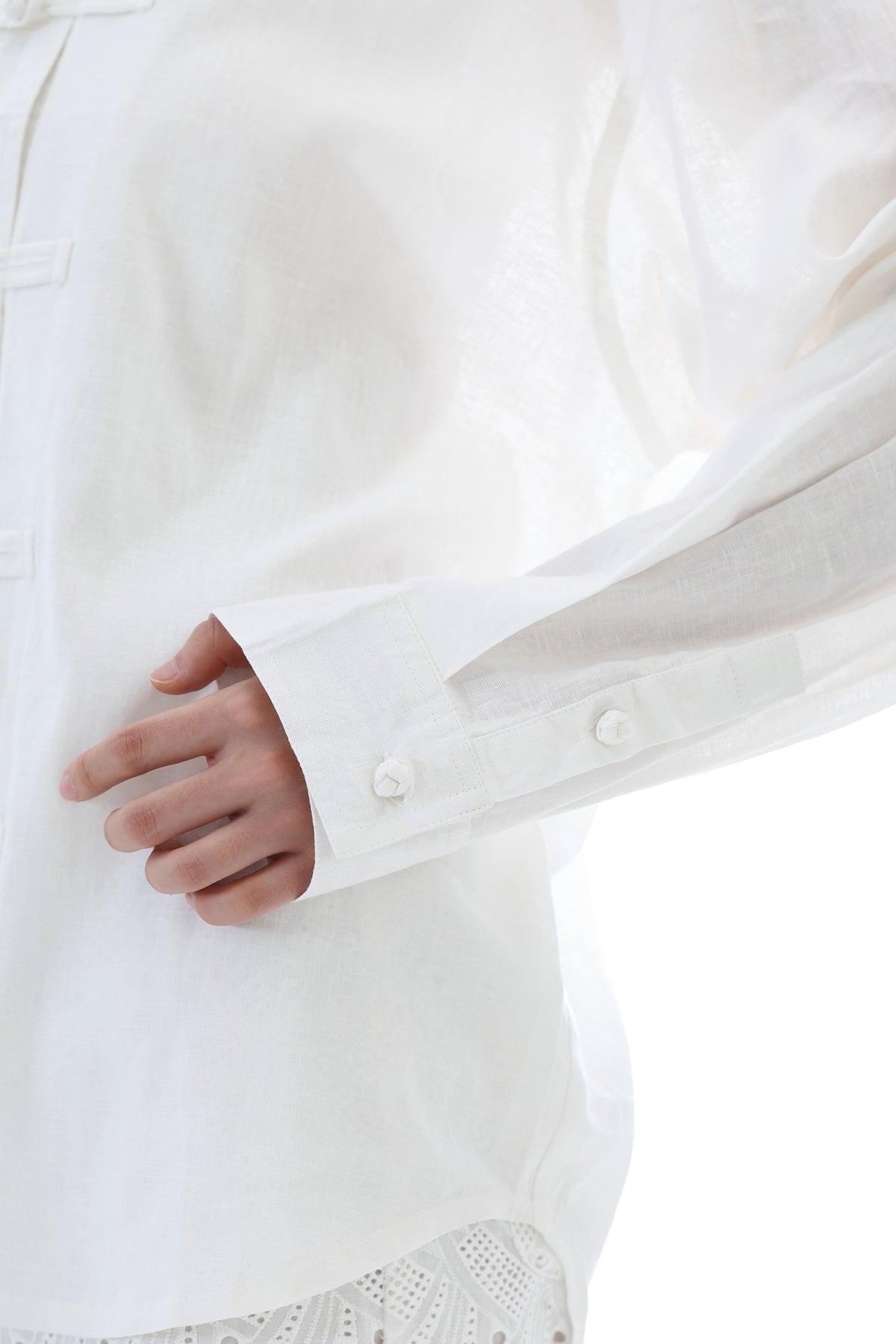 Close-up of a person wearing a white long-sleeve button-up shirt, showing the sleeve cuff with buttons and part of the hand.