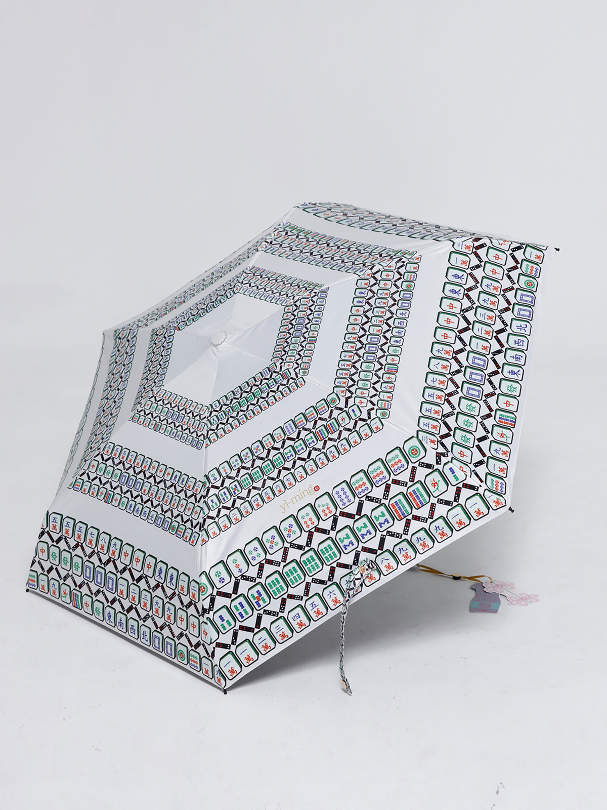A folding umbrella with a white base and an intricate geometric pattern in black, green, and red, shown on a light gray background.