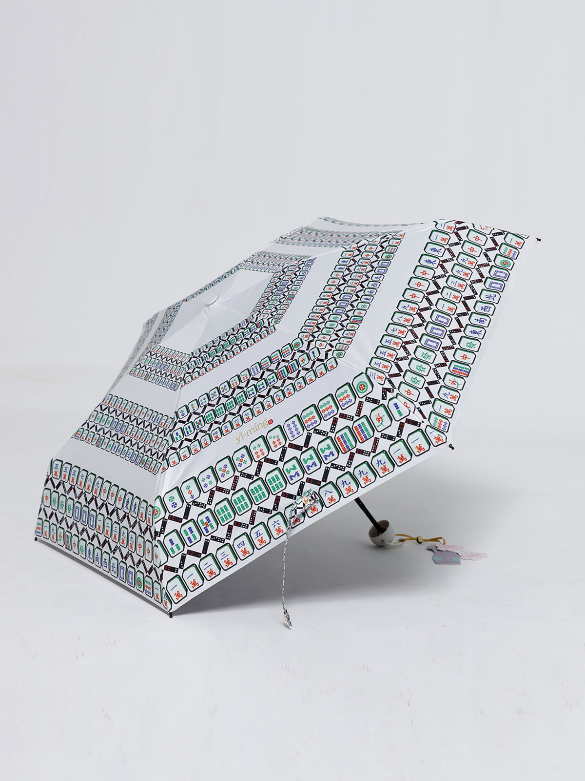 A folding umbrella with a white background and a colorful geometric pattern, shown on a light gray studio background.