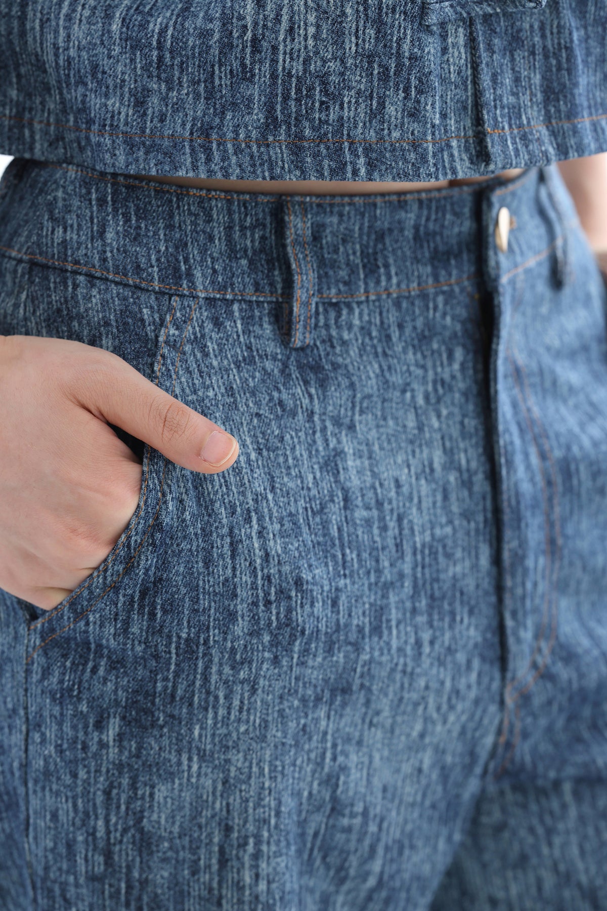Close-up of a person wearing blue denim jeans with a hand in the pocket, showing the fabric texture and waistband details.