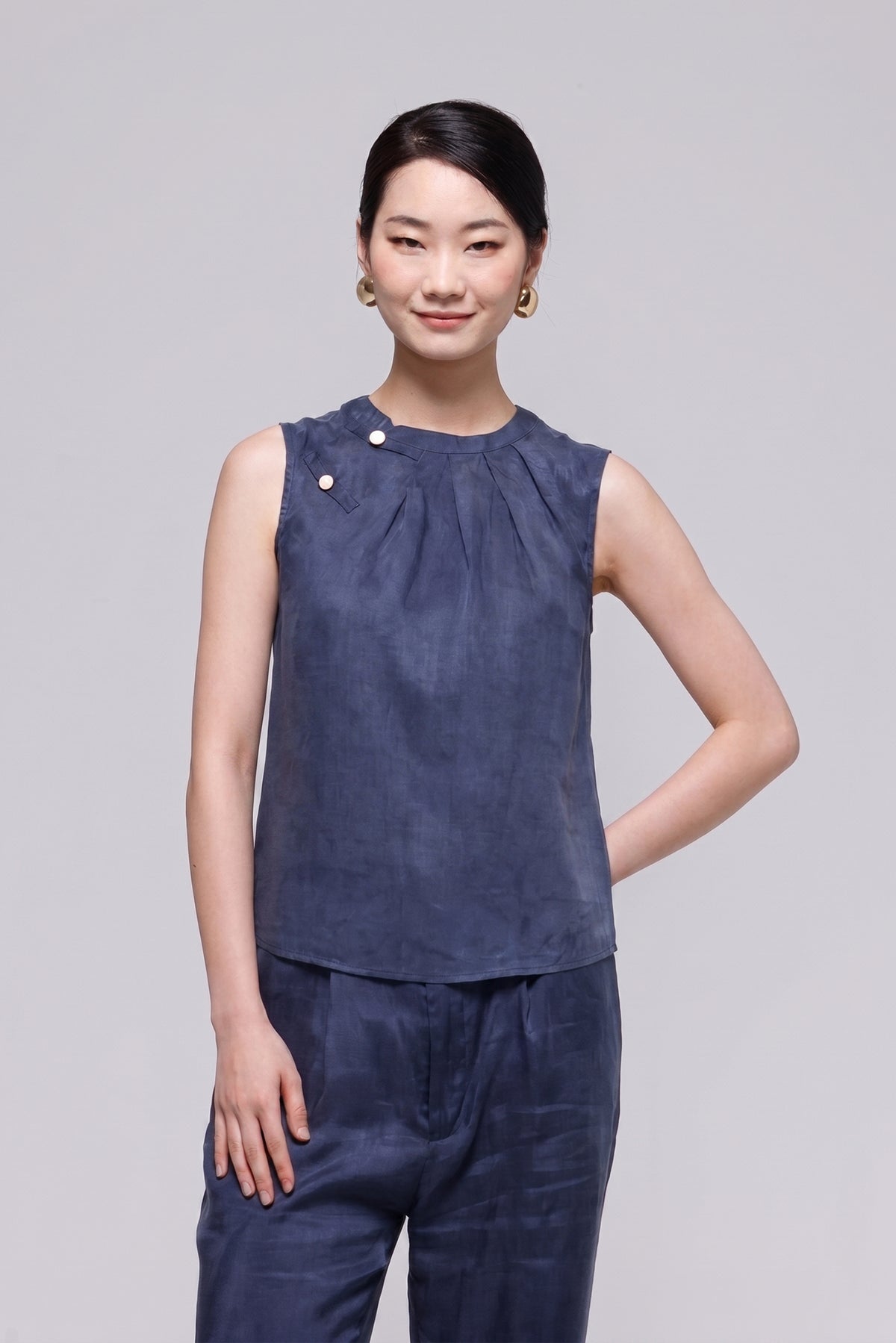 A woman modeling a sleeveless dark blue top and matching pants against a light gray studio background.
