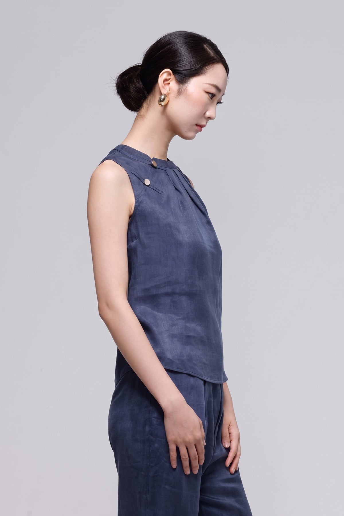 A woman in side profile wearing a sleeveless navy blue top and matching pants against a light gray studio background.